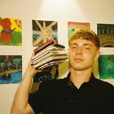 rockylevi holding a stack of records in front of a wall of paintings